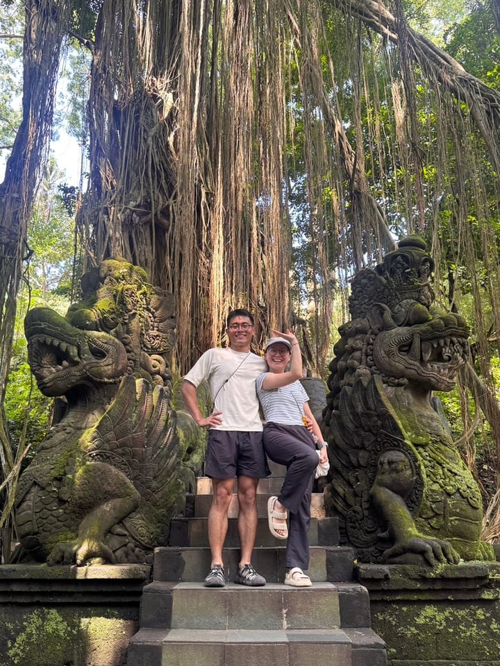 两人站在高大树根与石雕之间合影