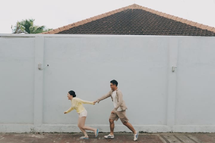 两人牵手沿白墙奔跑
