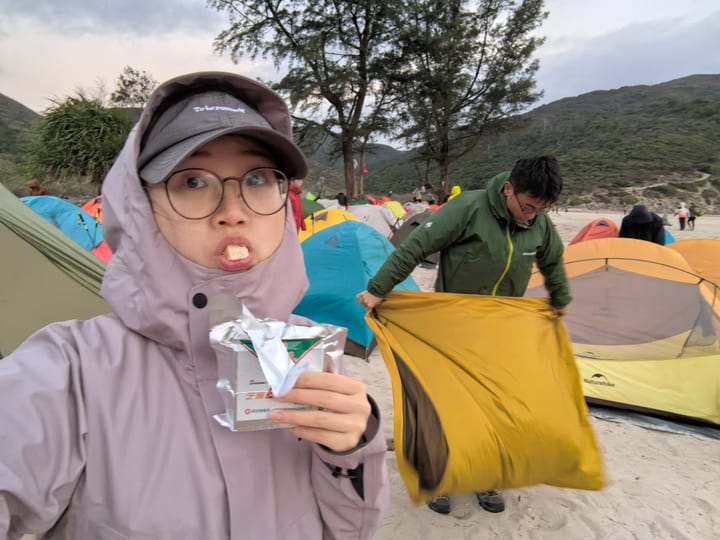 一人在帐篷旁吃早餐，另一人在身后整理营地